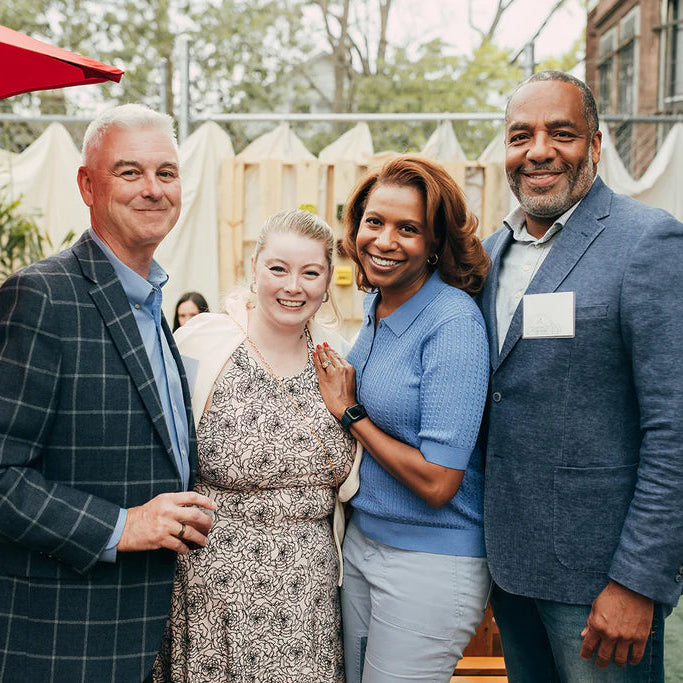 Group of four people smiling and posing together outdoors with a red umbrella  during the preview party fundraiser.