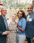 Group of four people smiling and posing together outdoors with a red umbrella  during the preview party fundraiser.