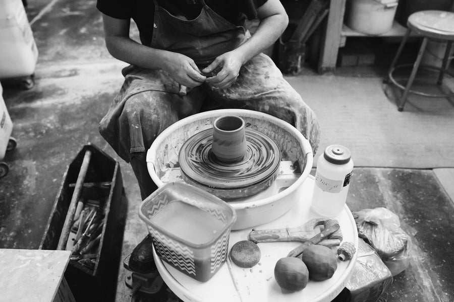 A Pewabic artisan leans back to look at their handiwork: a half-formed cup made of wet clay on their potters wheel.