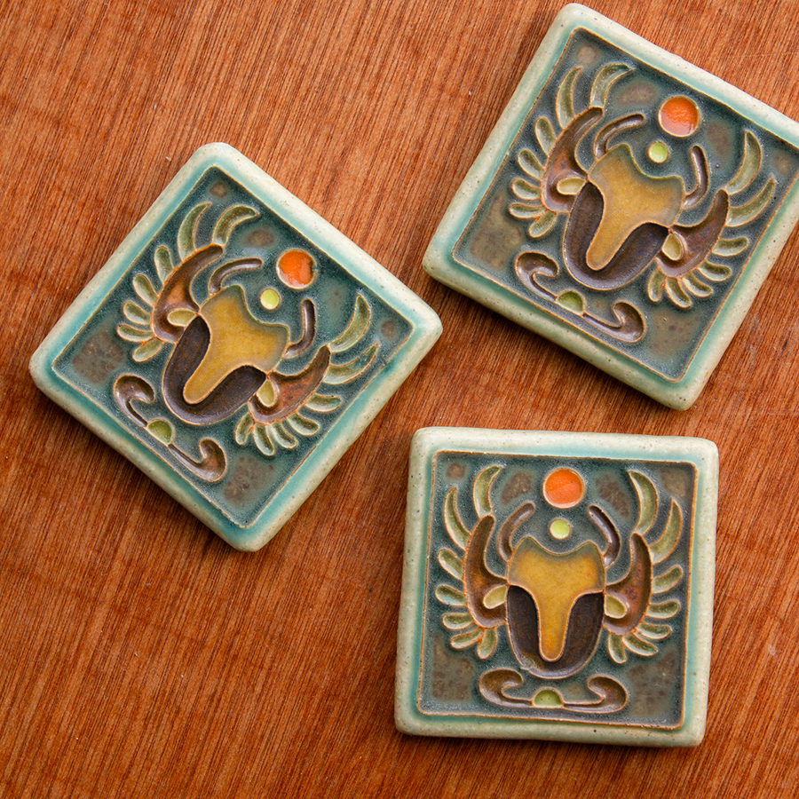 This hand painted tile features a scarab is multiple brown colors on a background of the crystalline, shimmering deep green Viridian glaze with a pale blue border.