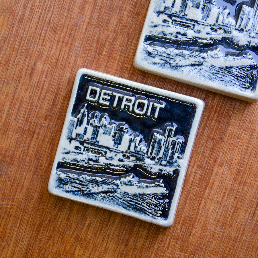 This two-tone Detroit Skyline tile is featured in the Viridian/Scrape color palette. The sky and water are in a shiny black glaze while the skyline, boat, and word are a creamy white color.