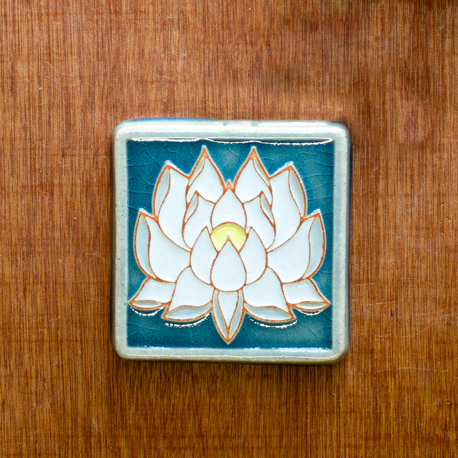 This Hand-painted Lotus Tile features white petals and a yellow center on the flower which sits on a deep blue background.