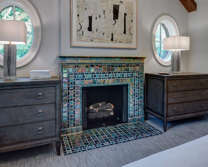 A Pewabic tile fireplace in a large bedroom is made of many shades of blue and green tiles in square shapes.