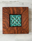 The Journey Knot Tile features two long ovals that create an x pattern with a large ring entwined with them. This tile is in our matte turquoise Pewabic Blue glaze which is beautifully offset with the deep reddish brown oak wood frame.