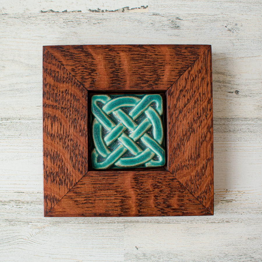 The Journey Knot Tile features two long ovals that create an x pattern with a large ring entwined with them. This tile is in our matte turquoise Pewabic Blue glaze which is beautifully offset with the deep reddish brown oak wood frame.