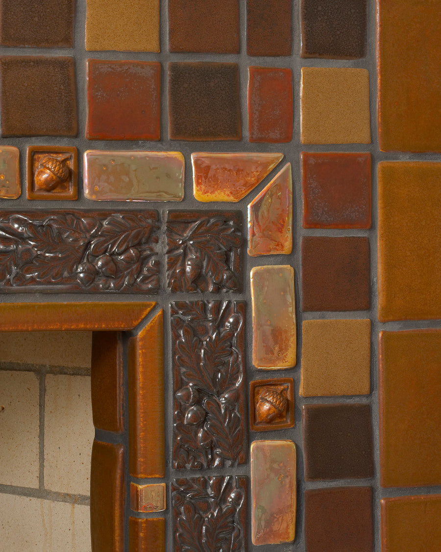 This fireplace tile is rustic and comprised of a blend of brown and earth-tone tiles. A tasteful Iridescent custom-cut trim lines the border alongside brown tiles in an acorn motif.