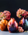 Three Copper glazed Teardrop vases stand filled with bushy hydrangea stems. The glaze on these vases have a rosy, purple and blue variation.