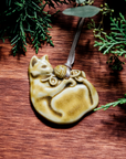 The ceramic Cat with Yarn Ornament features a cat on its back with its paws grasping a ball of yarn. Its face is happy and playful. Both the cat and the yarn are featured in our matte yellow-cream Wheat glaze.