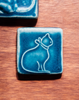 The ceramic cat tile design features the outline of a cat's full body in profile. The cat is wearing a collar with a bow in the back.