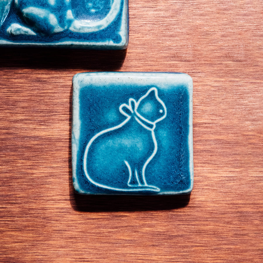 The ceramic cat tile design features the outline of a cat's full body in profile. The cat is wearing a collar with a bow in the back.