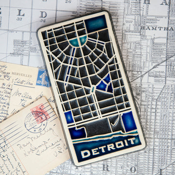 This rectangular Detroit Map Tile has a line drawing of the areal street view of downtown Detroit. The word "Detroit" is written at the bottom of the design.