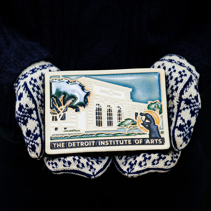 Two mittened hands hold the Detroit Institute of Arts tiles on a black background. 