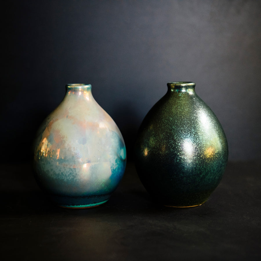 Two Teardrop vases feature the extremely variable Matte Green Iridescent glaze. One vase has a shiny blue-green metallic finish while the other has a matte, flat appearance similar to brushed metal.