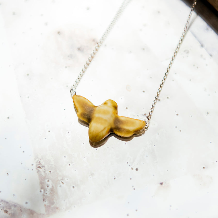 The matte Mustard colored bee pendant is attached to a silver chain.