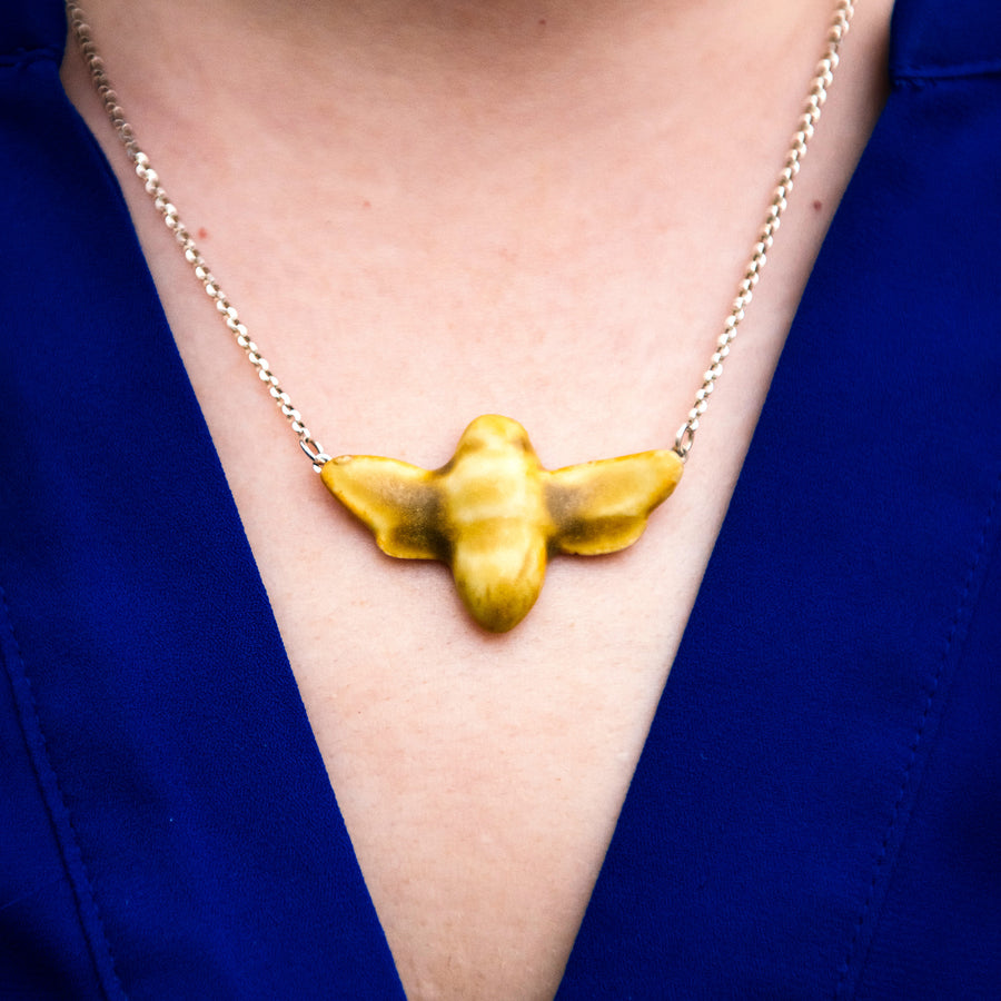 Close up photo of a woman wearing our historically inspired ceramic Bee Necklace in a matte Mustard glaze with a royal blue blouse.