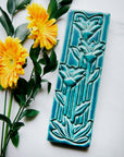 This large Floral Tile features three tall art deco-esque flowers on long straight stems with pointed leaves.