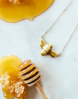 The Honey Gloss bee pendant is attached to a silver chain and sits next to a honey dipper.