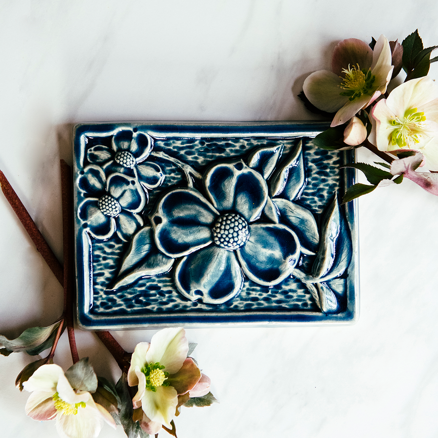 The Dogwood Tile features a blooming branch from a Dogwood tree- the three large flowers have four petals each with a bumpy circular center. 