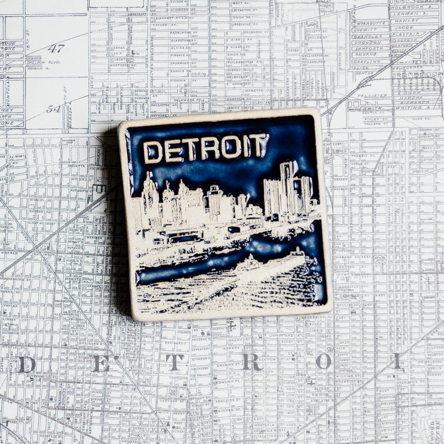 The Detroit Skyline tile features the current downtown skyline with the Detroit River in the foreground. A freighter floats by causing ripples on the otherwise flat surface of the water. The word "Detroit" is written above in the sky. This tile is in the two tone Midnight/Scrape option. The sky and water are in the glossy deep dark blue Midnight glaze while the skyline, boat and word is scraped to make a creamy white color.
