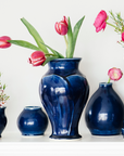 A glossy blue Midnight glazed Classic vase sits among similarly glossy pieces on a stark white mantel.