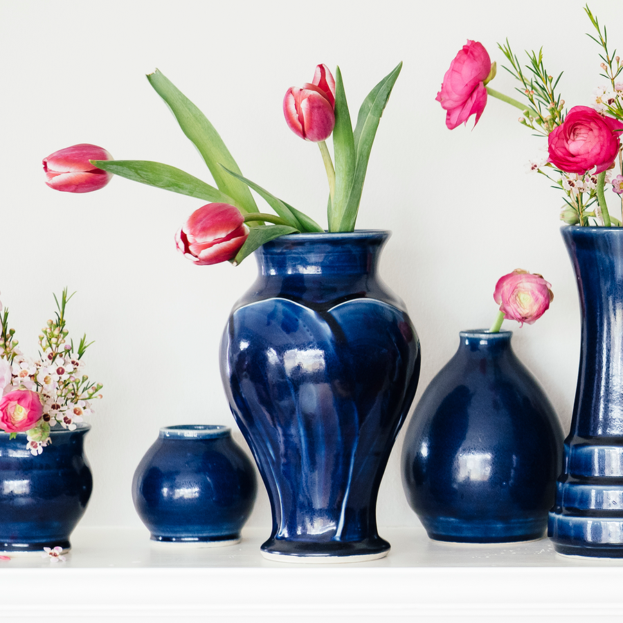 A glossy blue Midnight glazed Classic vase sits among similarly glossy pieces on a stark white mantel.