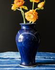 The Large Classic Vase starts with a small diameter at its base that gradually gets larger until it contracts again near the top with a slightly wider lip. The sides of the vase have been swiped with slip, this gives the appearance of abstract petals overlapping on the widest part of the vase. This Classic Vase features the glossy deep dark blue Midnight glaze.