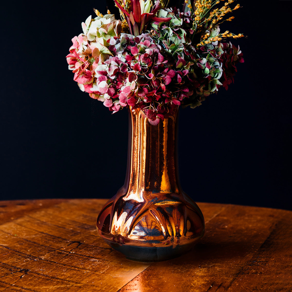 The Celtic Vase's base starts out wide and round at the bottom then becomes a straight pillar as it continues upward with a winding line design that has no beginning or end. The Copper iridescent glaze is a shiny, smooth metallic glaze with many variations. Some pieces end up with a blue-gray flashing of color that covers a portion of the surface.