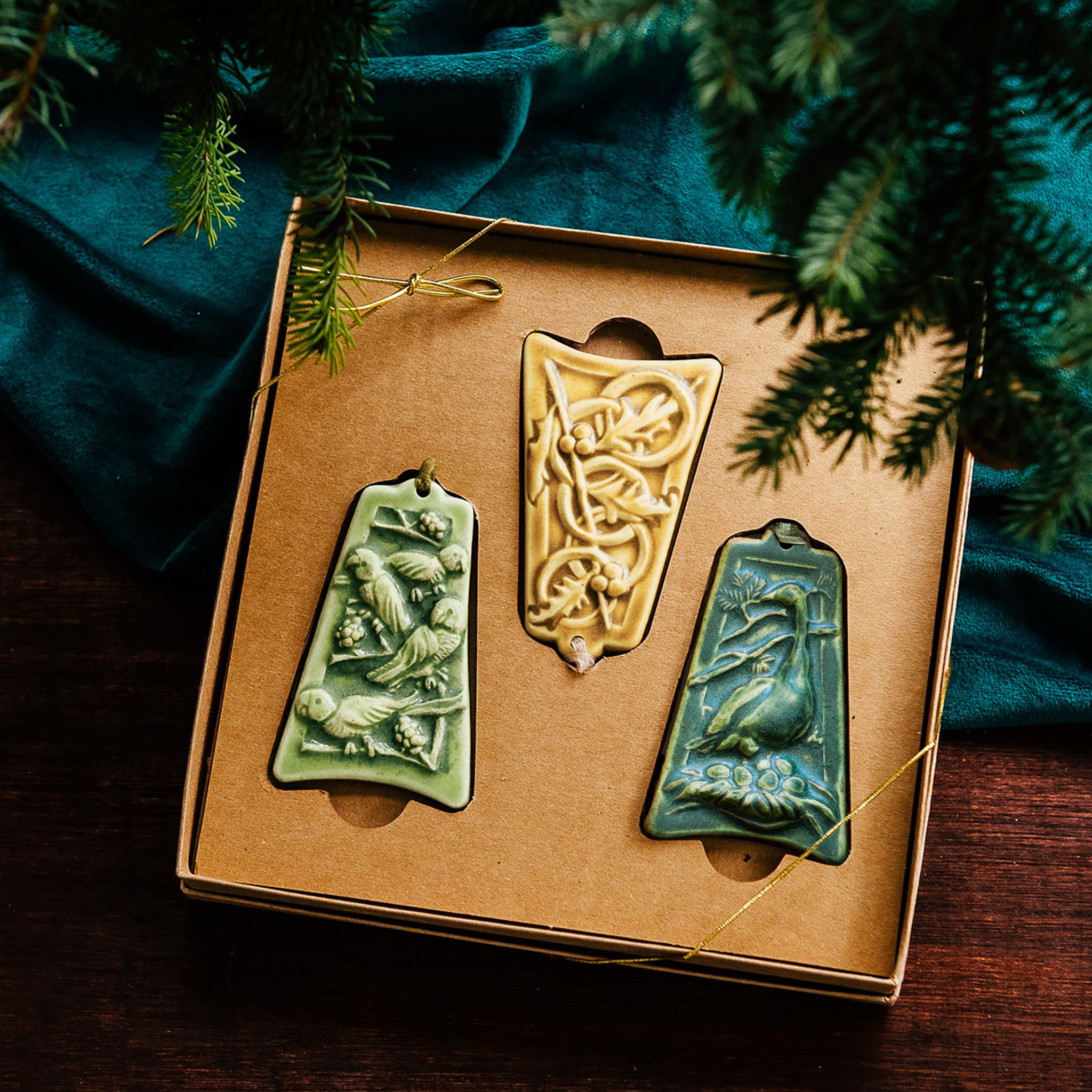 Three ceramic ornaments are sitting in a gift box and placed under a Christmas tree.