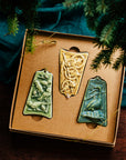 Three ceramic ornaments are sitting in a gift box and placed under a Christmas tree.