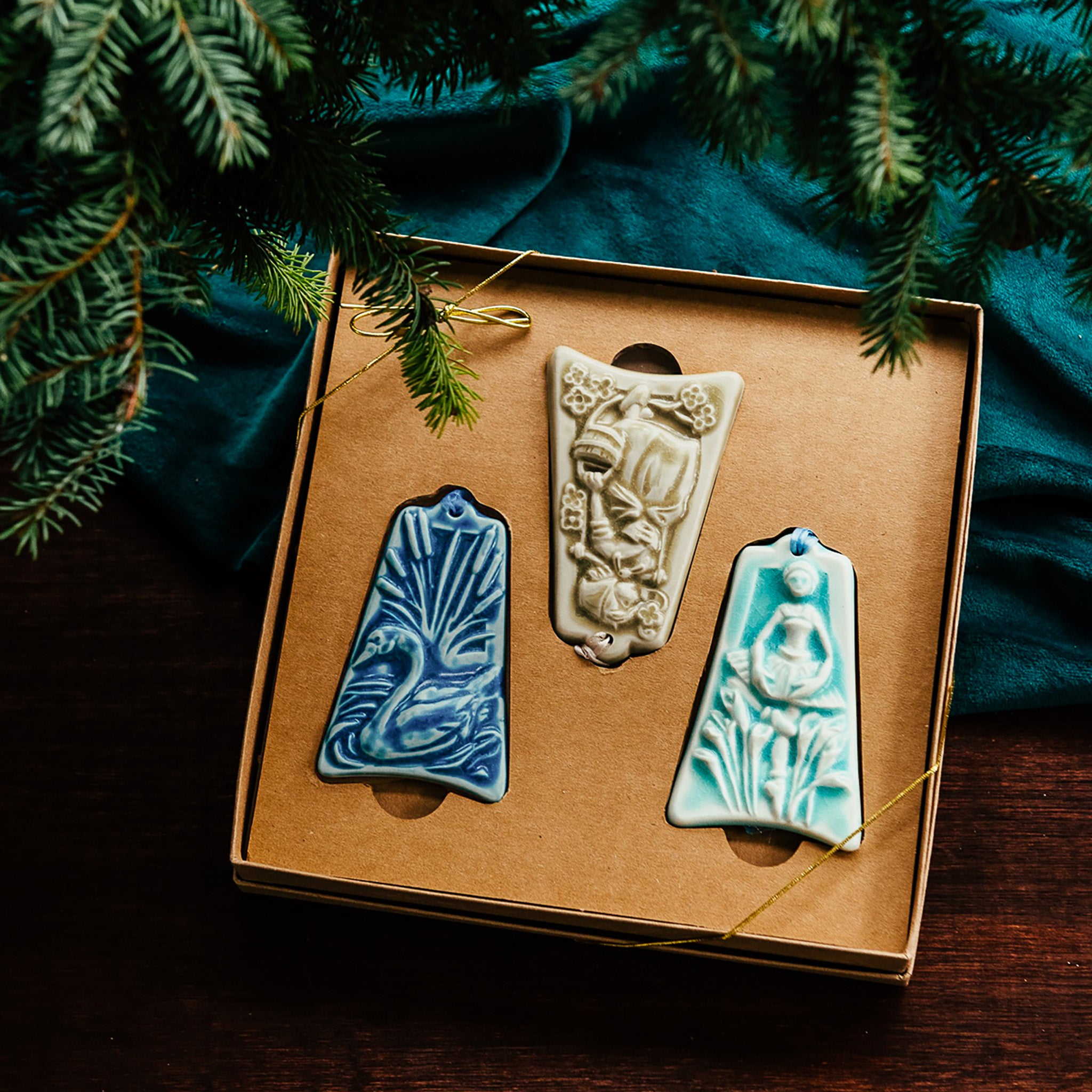 Three ceramic ornaments are sitting in a gift box and placed under a Christmas tree.
