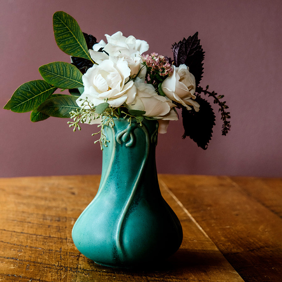 The Snowdrop vase has a wide, round base that contracts into a pillar as it gets taller. The rim of the vase has small snowdrop flowers whose stems glide gracefully down the sides of the vase.