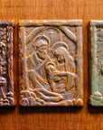 The Nativity Tile features the haloed holy family - Joseph, Mary and Baby Jesus - embracing under the wooden beams of the stable. Behind them, a window in the stone wall gives a glimpse of the Bethlehem star. This tile features the pinkish gold metallic Blush Iridescent finish which has many variations. Depending on the lighting in the room, these pieces will pick up different hues.