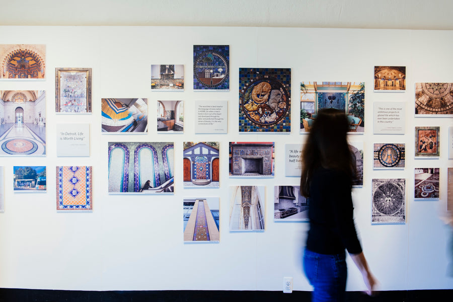 A woman walks through the museum in our historic building past a wall full of images of Pewabic tile installations. 