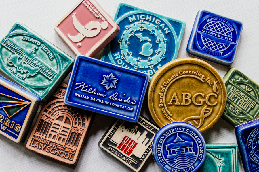 A display of commemorative tiles are spread across a white table top. They come in all shapes, sizes, and colors.
