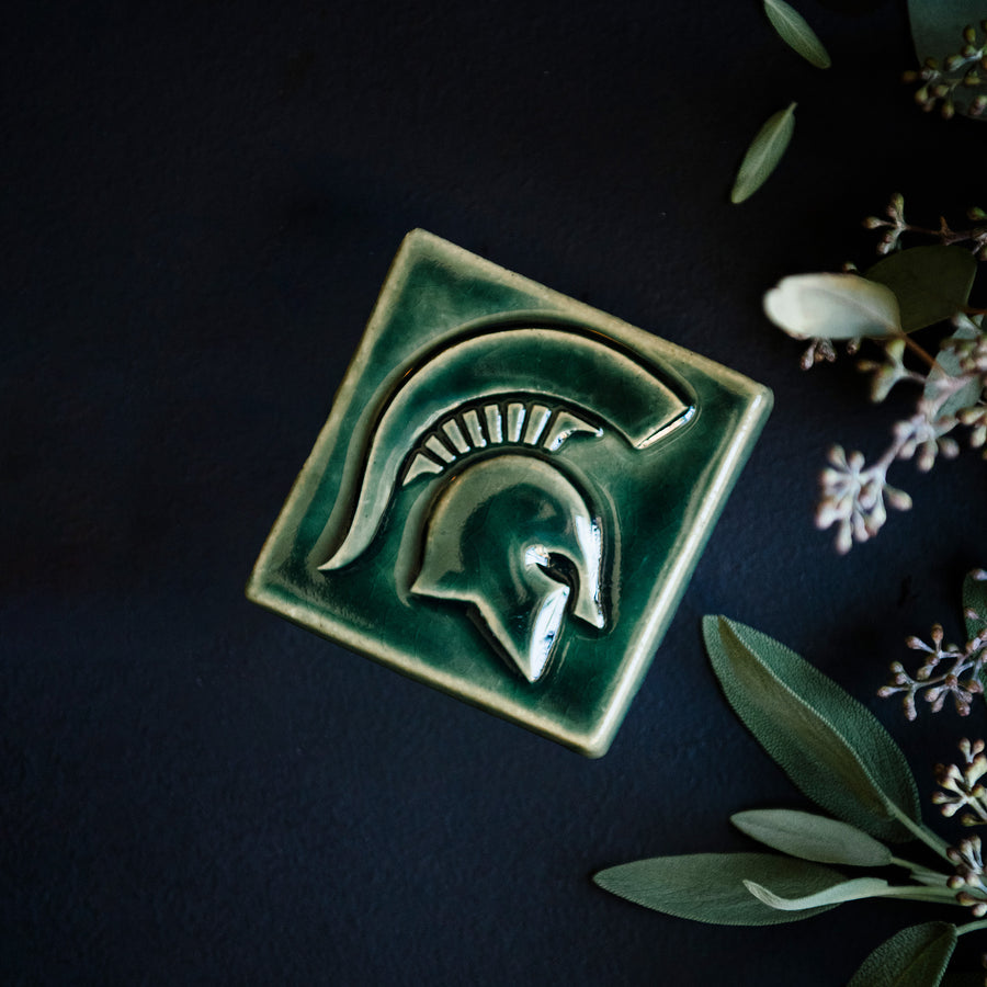 A Kale colored tile rests on a table with seeded eucalyptus bordering it.