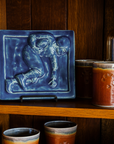 A deep matte blue Lagoon glazed 8x8 tile featuring a high relief sculpted tile of a football player holding the ball in the starting lineup position