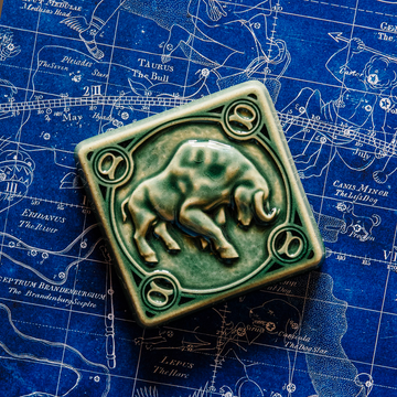 The Taurus tile in emerald glaze sits on a vintage blue and white map of the celestial sky.