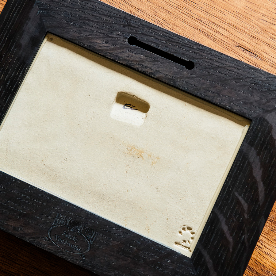 Our framed, hand-painted Detroit Flag Tile is laying on the historic Pewabic tiled floor in our upstairs gallery space, face down. You can see the built-in hanger pressed into the ceramic tile and the initials "LMP" of the Pewabic artist who painted the tile. These tiles are a rustic brown and tawny in appearance.