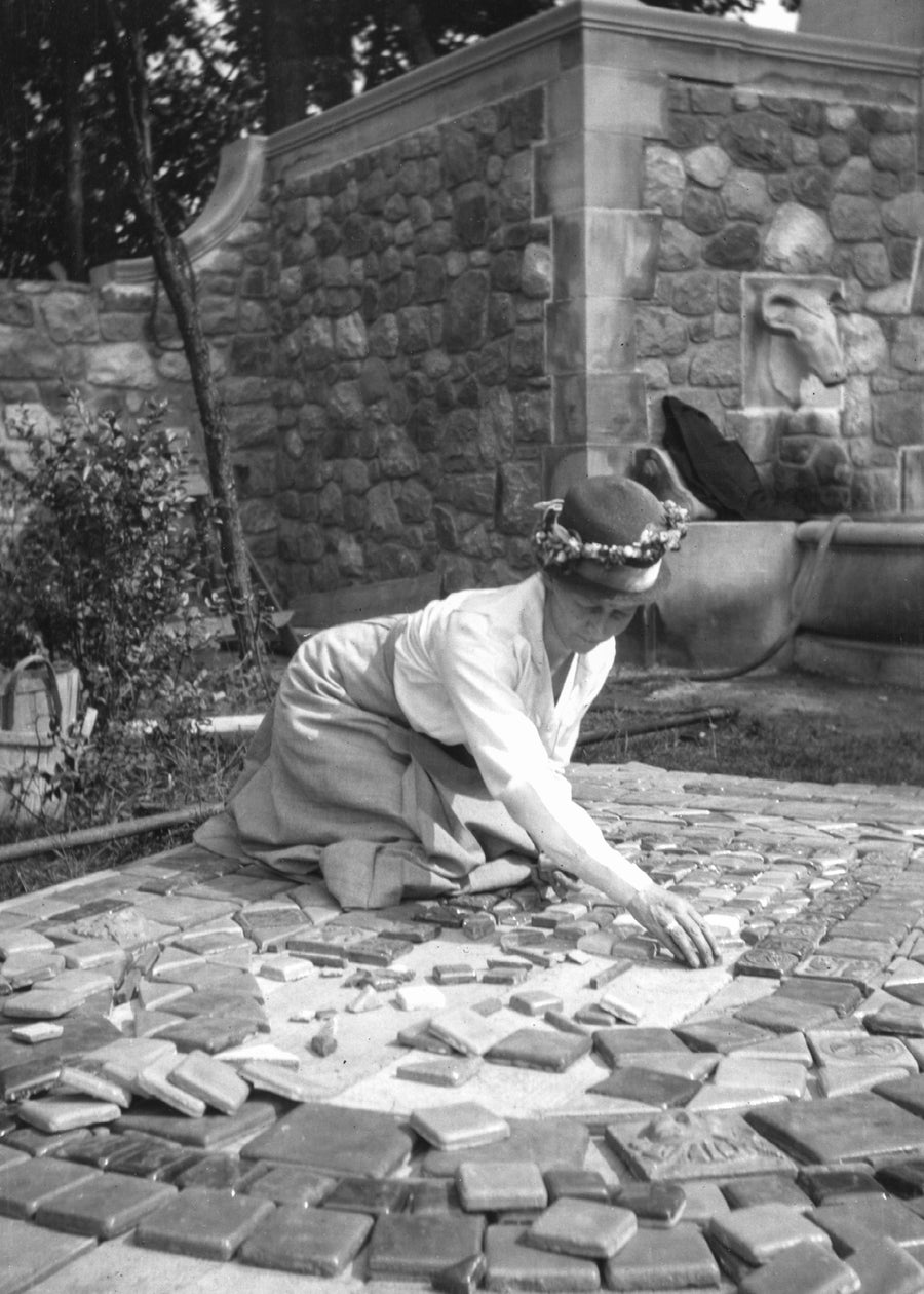 A historic image of Mary Chase Perry Stratton as she sits on the ground and lays out tiles for an outdoor fountain.