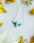 The blue Glacier Gloss glazed bee pendant is attached to a silver chain.