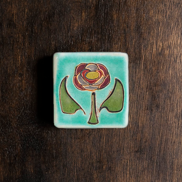 The Hand-Painted Rose Tile features a line drawing of a pinkish dusty rose in the center with a green stem and leaves on a pale blue background.