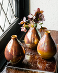 Three Teardrop vases sit on a windowsill. They feature the pinkish gold Blush Iridescent glaze.