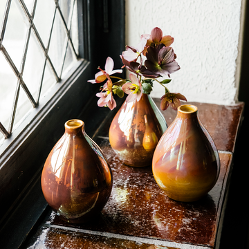 Three Teardrop vases sit on a windowsill. They feature the pinkish gold Blush Iridescent glaze.