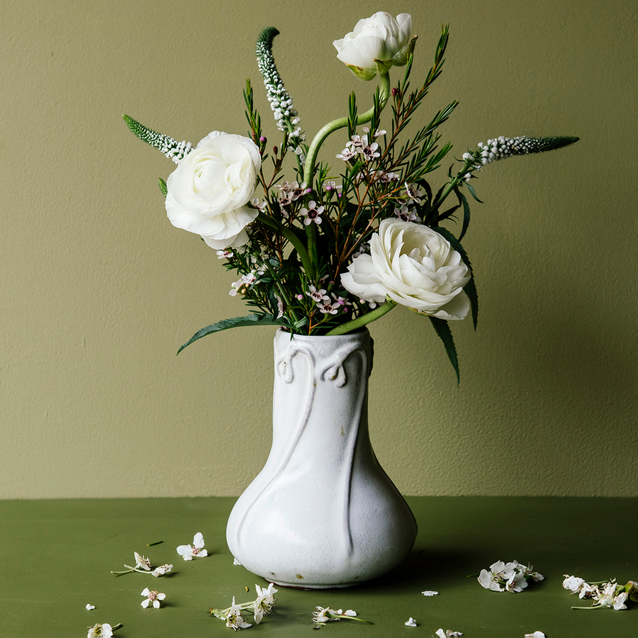 The Snowdrop vase has a wide, round base that contracts into a pillar as it gets taller. The rim of the vase has small snowdrop flowers whose stems glide gracefully down the sides of the vase.