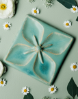The Flower Geo Tile features a four-petaled flower. Each petal takes up a quarter of the tile, making a perfectly geometric shape. The inner part of the flower is round with four cattail shaped stamen exploding from the center that point out to the corners of the tile.