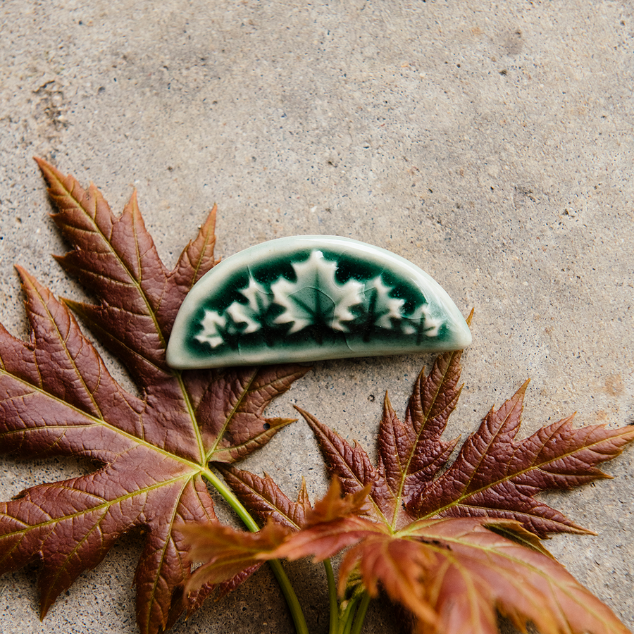 This Maple Leaf Pin is shaped like a half circle. It features five maple leaves in a fan-like formation with the largest in the center and smaller leaves flanking it at the sides.