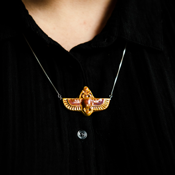 This high relief ceramic necklace features a stylized scarab with outstretched wings. The ends of each wing are attached to the silver chain.