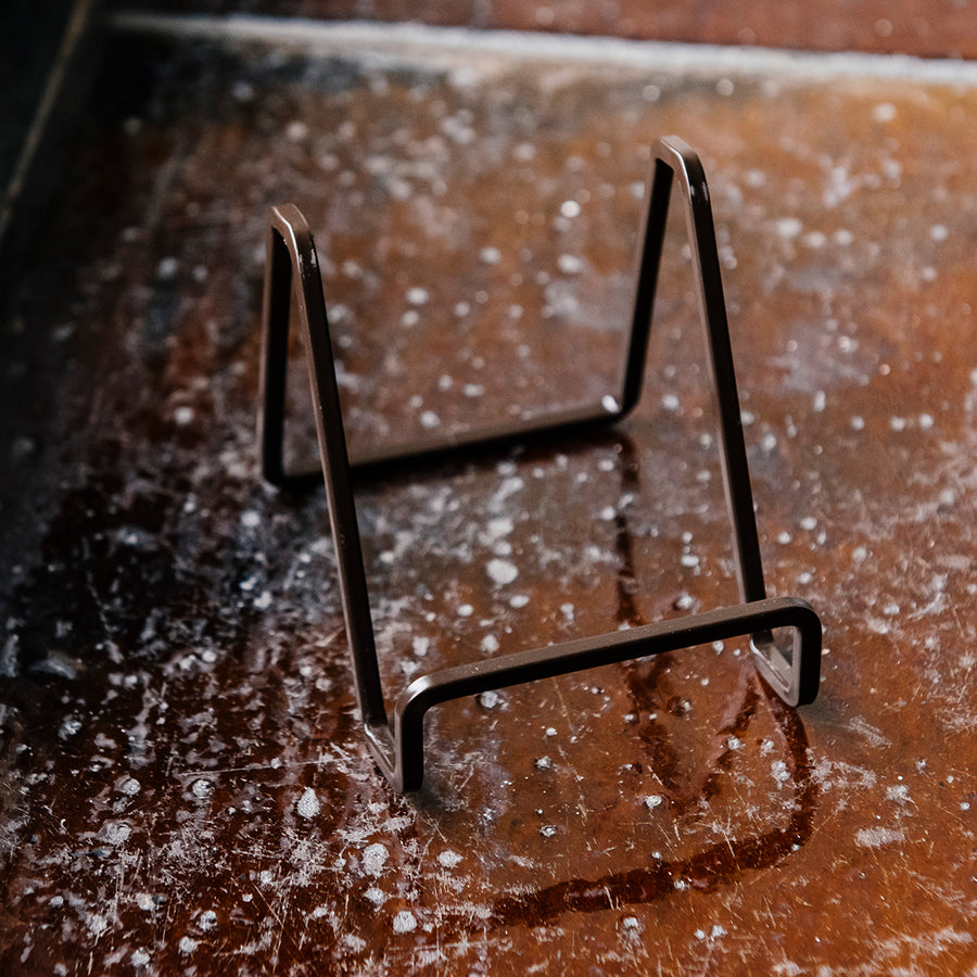 Detail photo of the matte bronze tile stand. It is empty and on a tiled-window ledge.