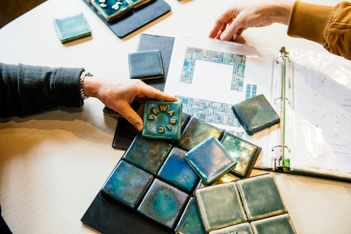 Blue Pewabic tile samples are displayed on a table with a portfolio folder.