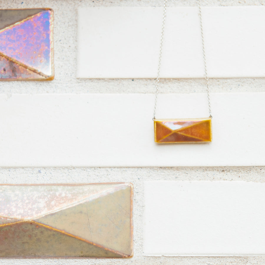 This necklace is resting next to the larger version of the pyramid design tile on the 2018 expansion of the Pewabic tile studio.